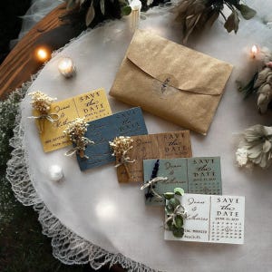 May include: A set of six save the date cards with different designs. The cards are decorated with dried flowers and greenery. The cards are all rectangular and have a white background. The text on the cards reads "Save the Date" and includes the names "James & Katherine" and the date "June 11, 2021".