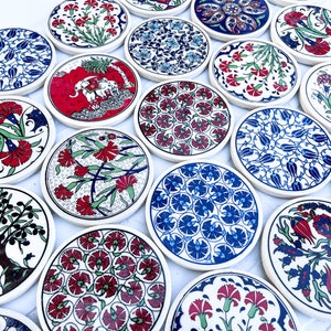 May include: A set of 15 round ceramic coasters with various colorful floral and geometric patterns. The coasters are white with blue, red, and green accents.