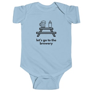 Op de afbeelding: Lichtblauwe baby romper met een zwarte illustratie van een picknicktafel met een bierglas en een babyfles erop. De tekst "Let's go to the brewery" staat onder de illustratie.
