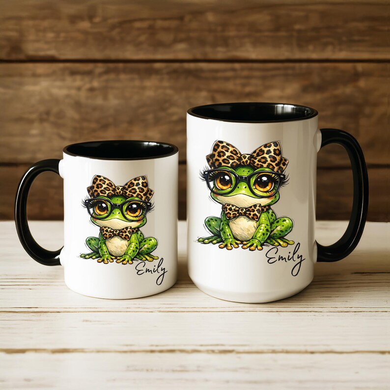 Puede incluir: Dos tazas de cer&aacute;mica blanca con interiores y asas negras. Cada taza presenta una rana de dibujos animados con gafas, pajarita y lazo, todo con un dise&ntilde;o de estampado de leopardo. El nombre "Emily" est&aacute; escrito en cursiva en cada taza.