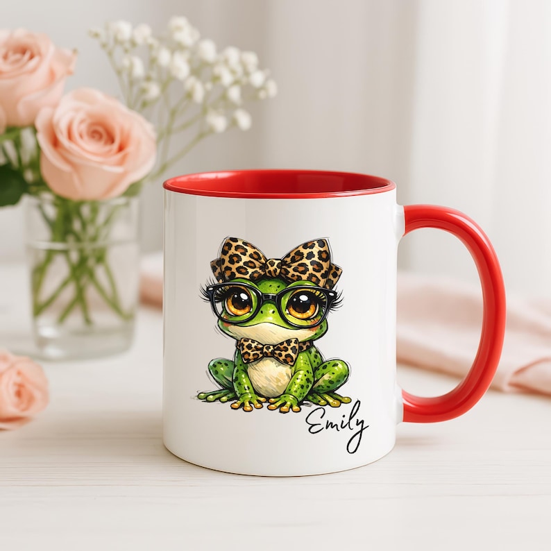 Puede incluir: Taza de cer&aacute;mica blanca con interior y asa rojos. La taza presenta una rana de dibujos animados con gafas, pajarita y lazo, todo con dise&ntilde;o de leopardo. El nombre "Emily" est&aacute; escrito en cursiva en la taza.