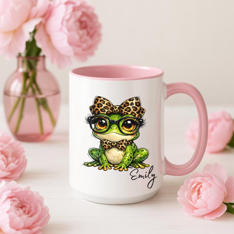 Puede incluir: Taza de cer&aacute;mica blanca con interior y asa rosas. La taza presenta una rana de dibujos animados con gafas, pajarita y lazo, todos con dise&ntilde;o de leopardo. El nombre "Emily" est&aacute; escrito en cursiva.