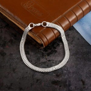 May include: A silver chain bracelet with a box clasp. The bracelet is made of multiple strands of chain.