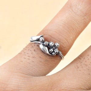 May include: A silver ring with a floral design featuring a cluster of small, round berries and leaves.