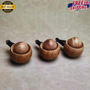 May include: Three car air freshener vent clips, each featuring a small, round, light brown wooden bowl containing a smooth, spherical wooden ball. The clips are black and attached to the back of each wooden bowl, designed for attachment to vehicle vents.