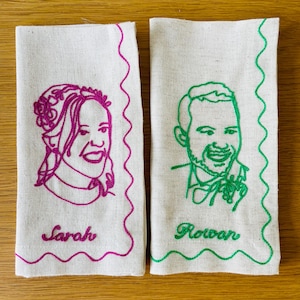 Puede incluir: Dos servilletas de lino blanquecino con retratos bordados. Una presenta un contorno magenta de una mujer con el nombre "Sarah" debajo. La otra tiene un contorno verde de un hombre con el nombre "Rowan". Ambas tienen un borde ondulado decorativo.