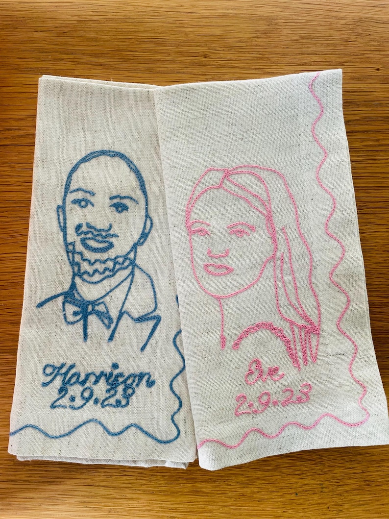 Puede incluir: Dos servilletas de lino con retratos bordados. Una presenta un contorno azul de un hombre con el nombre "Harrison" y la fecha "2.9.23". La otra tiene un contorno rosa de una mujer con el nombre "Eve" y la fecha "2.9.23".