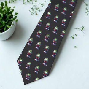 May include: A black necktie featuring a repeating pattern of small green frogs sitting inside red wine glasses. The tie has a pointed tip and a smooth fabric texture, displaying a consistent graphic print of the frogs across the entire surface.