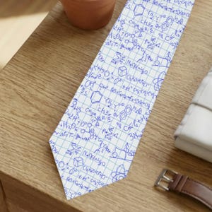 May include: A white necktie with a blue scientific formula pattern. The tie is lying on a wooden surface next to a white dress shirt, a wristwatch, and a small potted succulent plant.