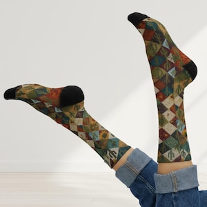 May include: A pair of patterned socks with a geometric design featuring diamonds, triangles, and cacti in shades of green, brown, red, and blue. The socks have black heels and toes. The person is wearing blue jeans.