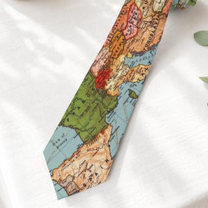 May include: A necktie featuring a vintage-style map print of Europe, displaying various countries in muted shades of green, tan, and red, with blue oceans and clearly labeled geographical names and political borders printed across the fabric surface.