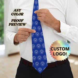 May include: A blue tie with a repeating white logo pattern. The tie is being held up by a person wearing a white shirt. Text on the image reads "ANY COLOR, PROOF PREVIEW" and "CUSTOM LOGO!"