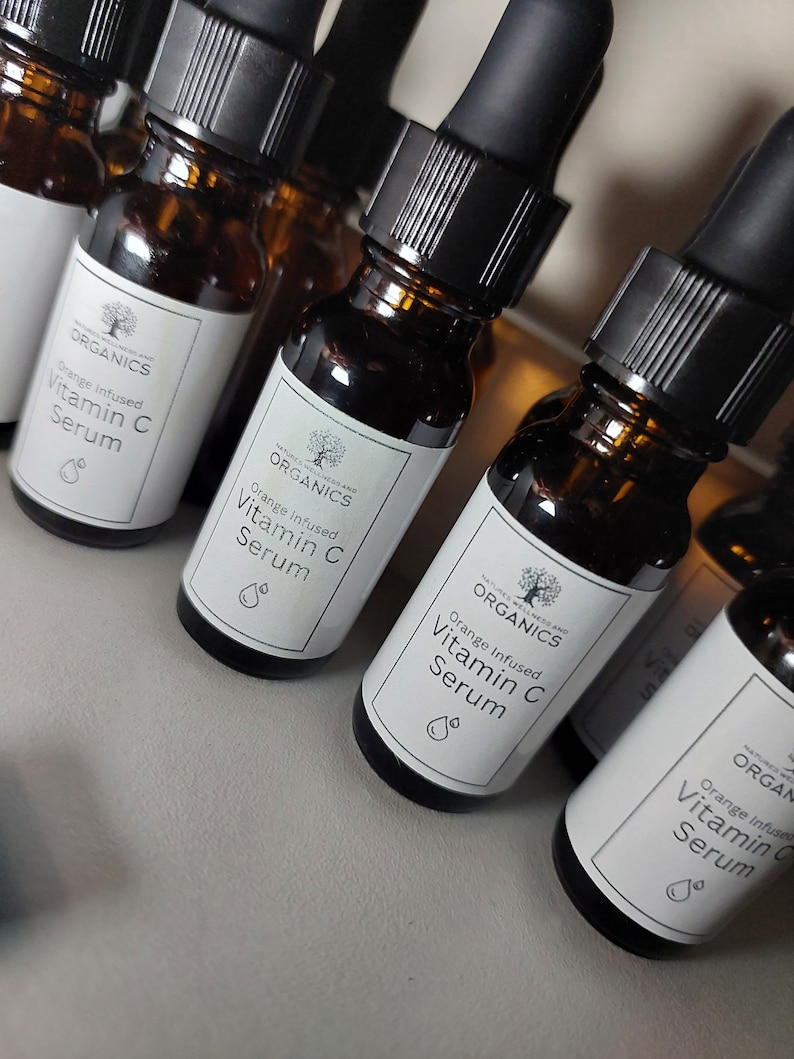 K&ouml;nnte beinhalten: Mehrere bernsteinfarbene Glasflaschen mit schwarzen Tropfern und wei&szlig;en Etiketten. Die Etiketten zeigen ein Baumlogo und den Text "NATURE'S WELLNESS AND ORGANICS" und "Orange Infused Vitamin C Serum".