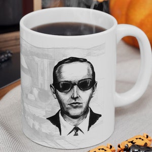 以下が含まれることがあります： 白いセラミック製のコーヒーカップに、サングラスをかけた男性の白黒のイラストが描かれています。カップには黒い取っ手が付いており、コーヒーでいっぱいです。カップは、オレンジと黒のキャンディーが置かれた白い表面の上に置かれています。