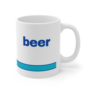 May include: White ceramic mug with the word "beer" in blue lettering. A horizontal blue stripe with a darker blue border is near the bottom of the mug. The mug has a curved handle.