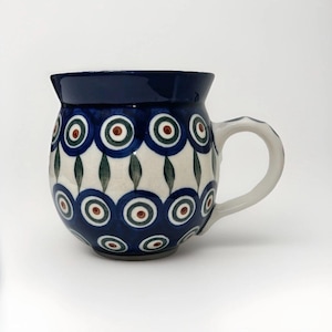May include: A ceramic mug with a rounded body and a dark blue rim and handle. The mug features a repeating pattern of blue circles with red and green accents on a white background. The handle is white.