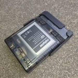 Puede incluir: Un dispositivo electr&oacute;nico rectangular negro y transparente con una bater&iacute;a y el texto "mobile" visible. El dispositivo est&aacute; sobre una superficie gris.