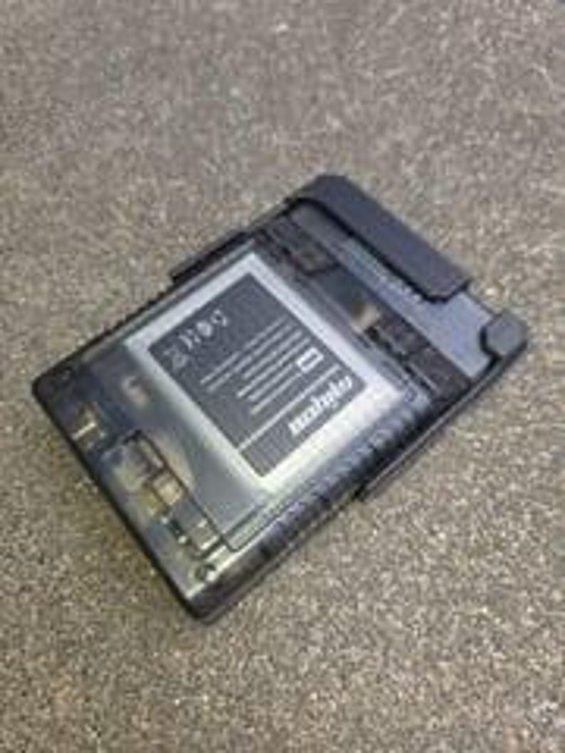 Puede incluir: Un dispositivo electr&oacute;nico rectangular negro y transparente con una bater&iacute;a y el texto "mobile" visible. El dispositivo est&aacute; sobre una superficie gris.