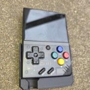 Puede incluir: Una consola de juegos port&aacute;til negra con pantalla y botones de control. La consola presenta un panel direccional, botones de acci&oacute;n de colores y un dise&ntilde;o elegante y moderno. El dispositivo se muestra sobre una superficie de color neutro.