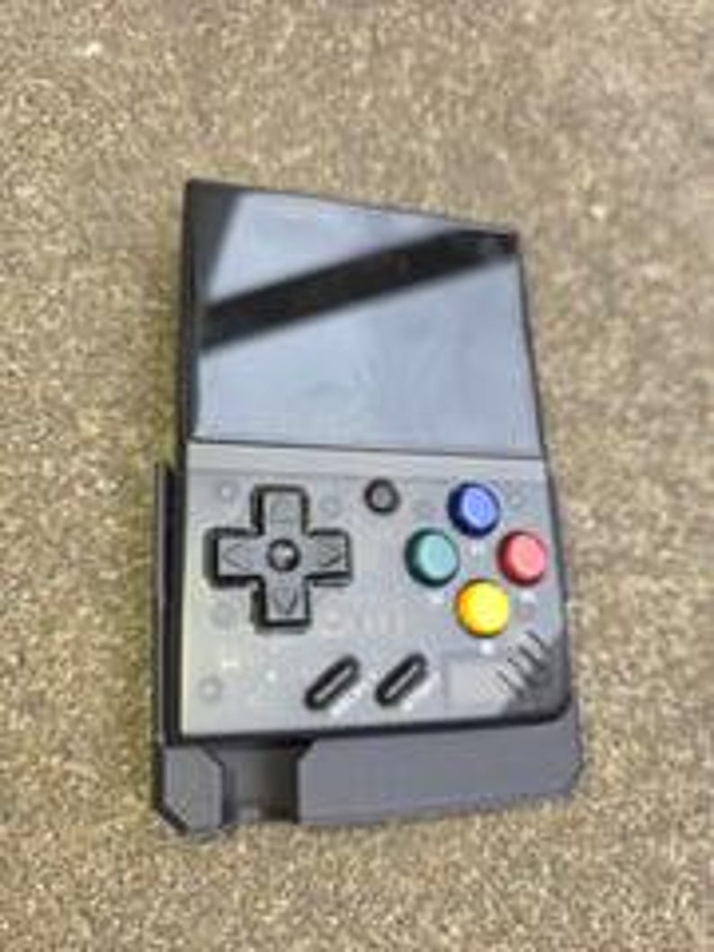 Puede incluir: Una consola de juegos port&aacute;til negra con pantalla y botones de control. La consola presenta un panel direccional, botones de acci&oacute;n de colores y un dise&ntilde;o elegante y moderno. El dispositivo se muestra sobre una superficie de color neutro.
