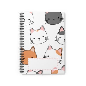 May include: A white spiral notebook with a colorful cat pattern. The cover features a variety of cats with different colored fur and facial expressions. The notebook has a blank label on the front.