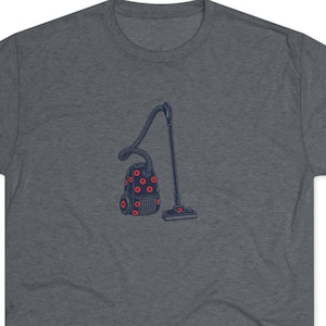 May include: A dark heather gray short-sleeve t-shirt featuring a centered graphic of a dark blue vacuum cleaner. The vacuum cleaner body is decorated with a repeating pattern of small, bright red circular shapes across its surface.