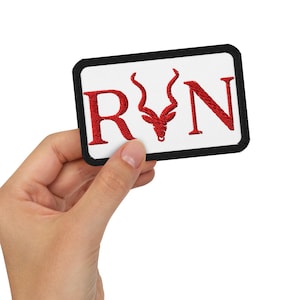 May include: Embroidered patch with the letters "RYN" in red, featuring a stylized antelope head in the center. The patch has a white background with a black border.