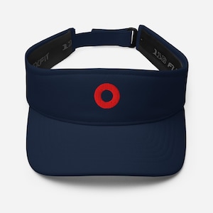 May include: A navy blue visor featuring a small, embroidered red circle on the front center. The visor has an adjustable strap with a black buckle at the back and interior branding that reads Flexfit 110 on the inner sweatband lining.