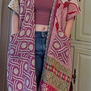 May include: A patchwork kimono jacket with short sleeves and pockets. The jacket features a mix of patterns in shades of red, purple, cream, and gold. The design includes geometric shapes and floral motifs, creating a bohemian aesthetic.