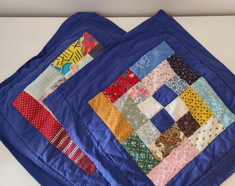 May include: Two square, blue throw pillows with patchwork quilt designs. One pillow features a vertical patchwork strip with red polka dots and other patterns. The other pillow has a central square patchwork design with various floral and geometric patterns.