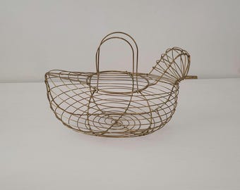 May include: A decorative wire basket in the shape of a chicken. The basket is made of gold-colored metal wire and features a handle and a tail. The basket is designed to hold eggs or other small items. The basket is a charming addition to any kitchen.