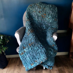 May include: A teal blue and brown chunky knit throw blanket draped over a chair. The blanket has a soft, fuzzy texture.