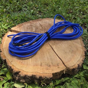 May include: A coiled blue rope with a black connector, secured with a black band, rests on a weathered, circular wooden tree stump. The scene is set outdoors with green grass and foliage.