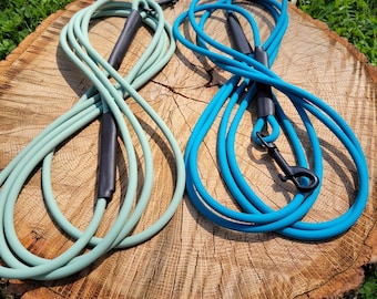 May include: Two dog leashes, one teal blue and one light green, are coiled on a wooden surface. Both leashes have black handles and clips.