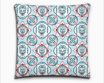 May include: A blue and white pillow with a repeating pattern of sugar skulls and floral designs. The skulls have red lips and are surrounded by white flowers.