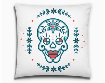 May include: A white pillow with a blue and red sugar skull design. The skull is surrounded by a wreath of blue leaves and red flowers.