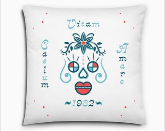 May include: White throw pillow with a blue and red stylized skull design, the text "Vitam Caelum Amare ~1982~" and red dots around the edges.