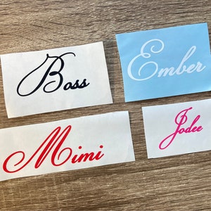 Może przedstawiać: Cztery białe karty z czarnym, czerwonym i różowym pismem ozdobnym. Karty zawierają napisy "Boss", "Mimi", "Ember" i "Jodee".