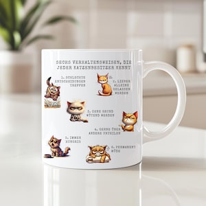 Könnte beinhalten: Weiße Keramiktasse mit sechs Cartoon-Katzen-Illustrationen und deutschem Text. Der Text beschreibt typische Katzenverhaltensweisen. Die Tasse hat einen gebogenen Henkel.