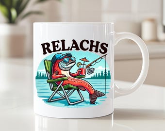 May include: White ceramic mug featuring a cartoon illustration of a red fish wearing sunglasses and a hat, relaxing in a chair with a drink. The mug has the word "RELACHS" in black letters.