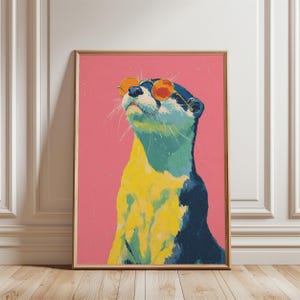 May include: A framed art print of an otter wearing orange sunglasses, set against a pink backdrop. The otter is depicted in yellow, blue, and black. The artwork is displayed in a room with white trim and a wooden floor.