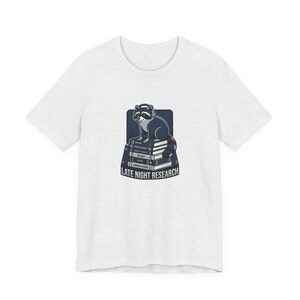 May include: A light gray t-shirt featuring a raccoon sitting on a stack of books. The raccoon is dark gray and white, with a blue background. The books have the words "Research", "Study", "Data", and "Knowledge" printed on them. The text "LATE NIGHT RESEARCH" is printed below the books.
