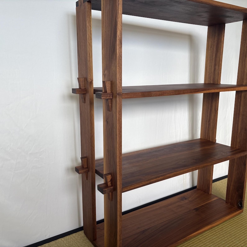 Peut inclure: Une &eacute;tag&egrave;re en bois brun fonc&eacute; avec trois tablettes. Les tablettes sont soutenues par des supports en bois visibles sur les c&ocirc;t&eacute;s de l'unit&eacute;.