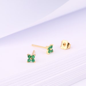 May include: A pair of gold earrings with a small green flower design. Each earring features a four-leaf clover shape with five green gemstones.