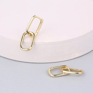 May include: Gold-toned double hoop earrings with a linked chain design. The earrings are shown on a white surface.