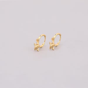 Peut inclure: Une paire de boucles d'oreilles créoles en or avec un charme en forme de palmier suspendu à chaque créole.