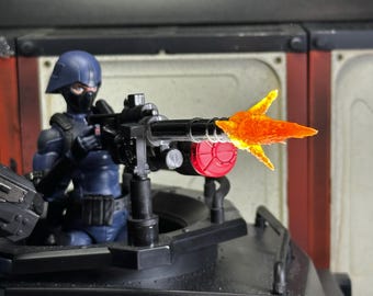 May include: A black action figure holding a black gun with an orange flame effect coming out of the barrel. The figure is wearing a black helmet and a blue uniform. The gun is mounted on a black vehicle.