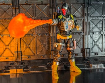 May include: Action figure of a futuristic warrior in a black and yellow suit, helmet with red visor, and a bright orange energy blast emanating from the right hand. The figure is posed against a metallic backdrop.