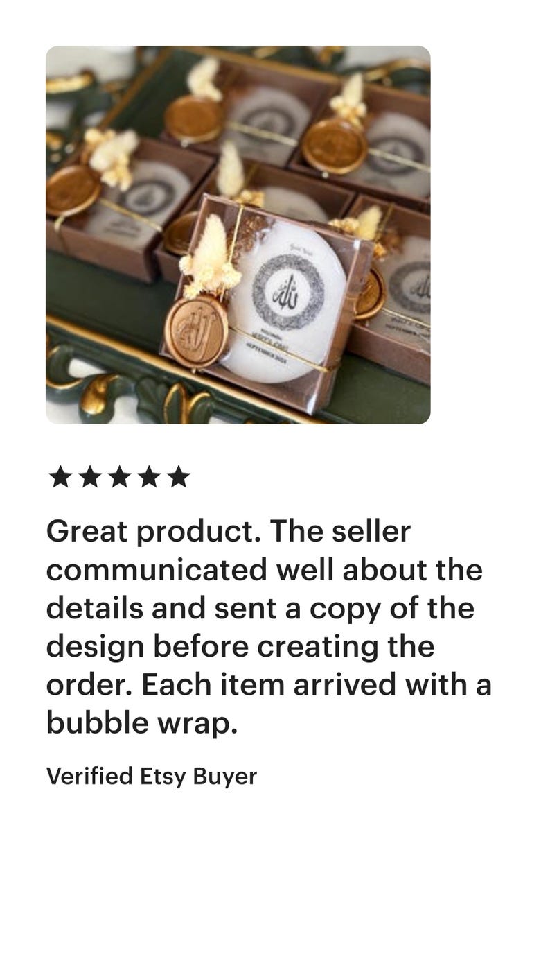 May include: A selection of white, round soaps in transparent boxes, each with a gold seal and decorative elements. The soaps feature a circular design with Arabic script. The boxes are on a green surface.