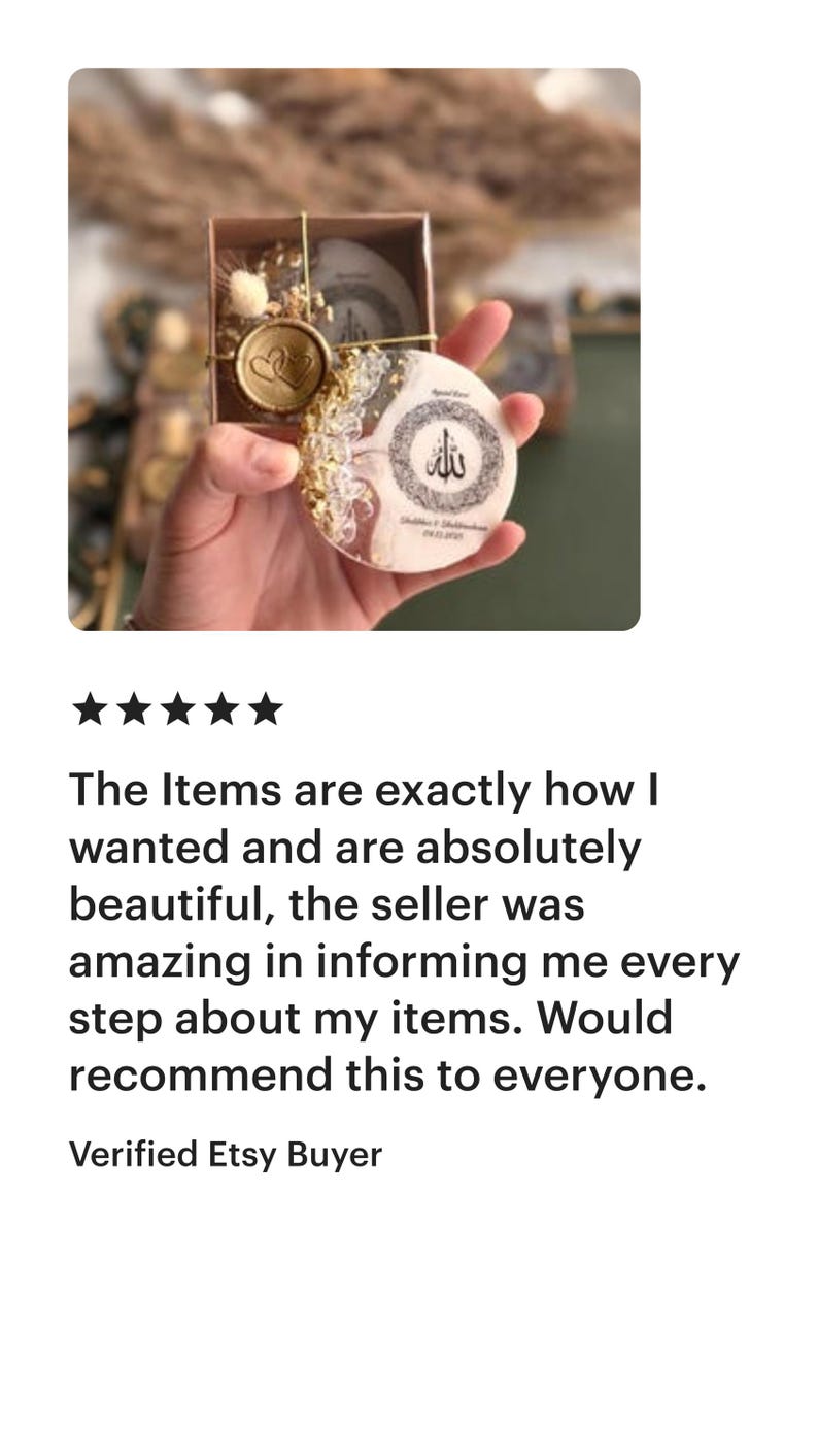 May include: A small, round decorative item with gold accents and a heart-shaped design, presented in a small box. The item has a white background with gold and glitter details. The item has Arabic text.